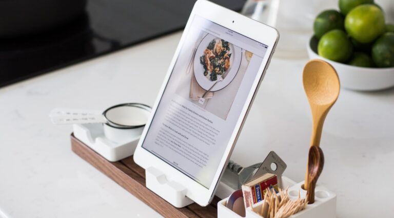 een tablet bovenop een tafel naast een houten lepel.