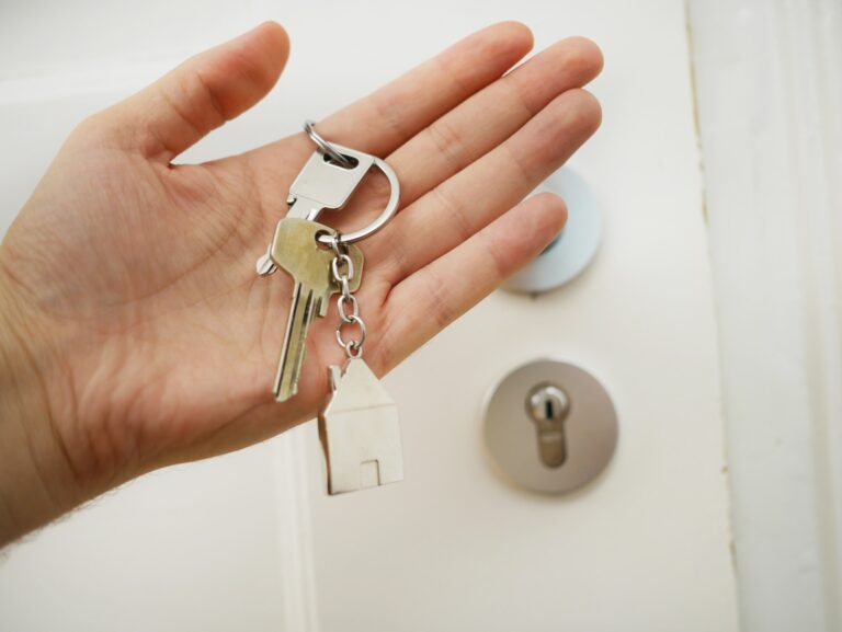 een hand die een sleutel van een deur vasthoudt.
