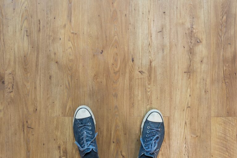 een persoon die op een houten vloer staat en blauwe sneakers draagt.